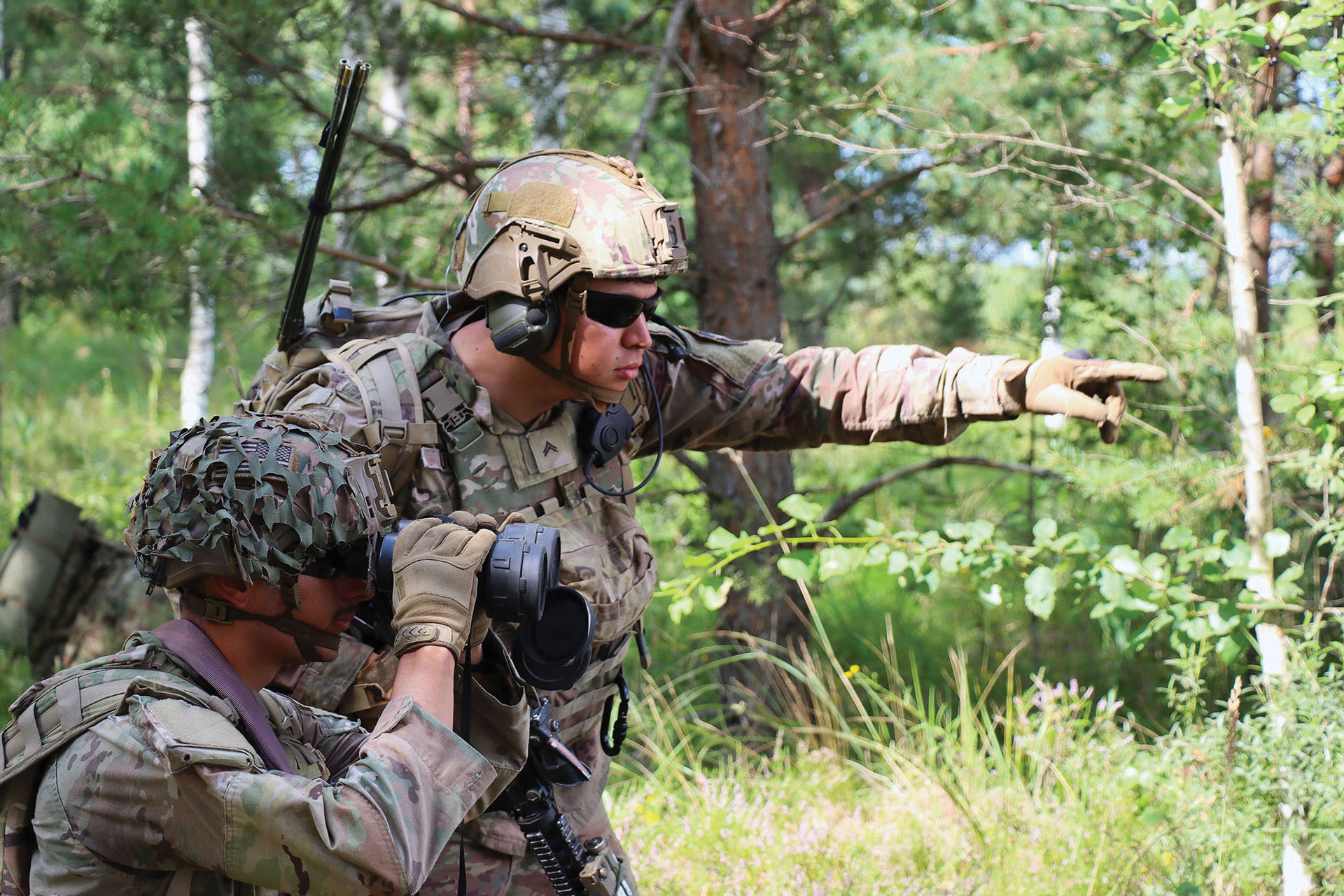 Soldado em camuflagem usando binóculos em uma área arborizada apontando para a frente
