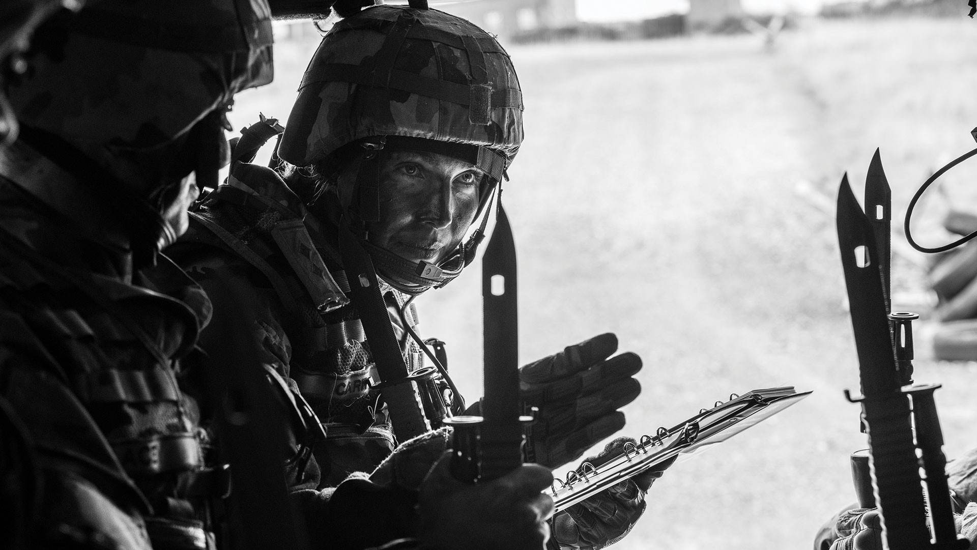 Una mujer soldado junto a otro soldado sostiene un cuaderno en una mano y apunta hacia adelante con la otra mano.