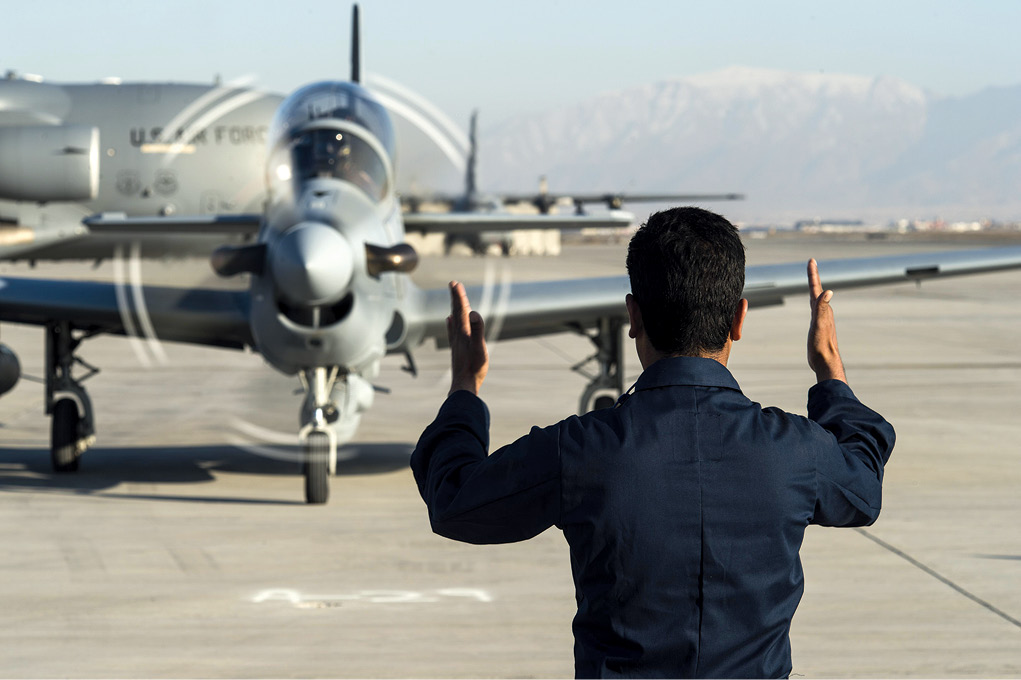 A member of the Afghan Air Force guides an A-29 Super Tucano 15 January 2016 at Hamid Karzai International Airport, Kabul, Afghanistan. The aircraft was added to the Afghan Air Force’s inventory in the spring of 2016. Designed to operate in high temperatures and in extremely rugged terrain, the A-29 Super Tucano is a highly maneuverable fourth-generation weapons system capable of delivering precision-guided munitions. (Photo by Tech. Sgt. Nathan Lipscomb, U.S. Air Force)