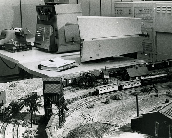 A model railroad train set is in the foreground with a DEC PDP-1 console and monitor sitting on a table in the background in the Tech Model Railroad Club in 1961. (Photo courtesy of the Computer History Museum)