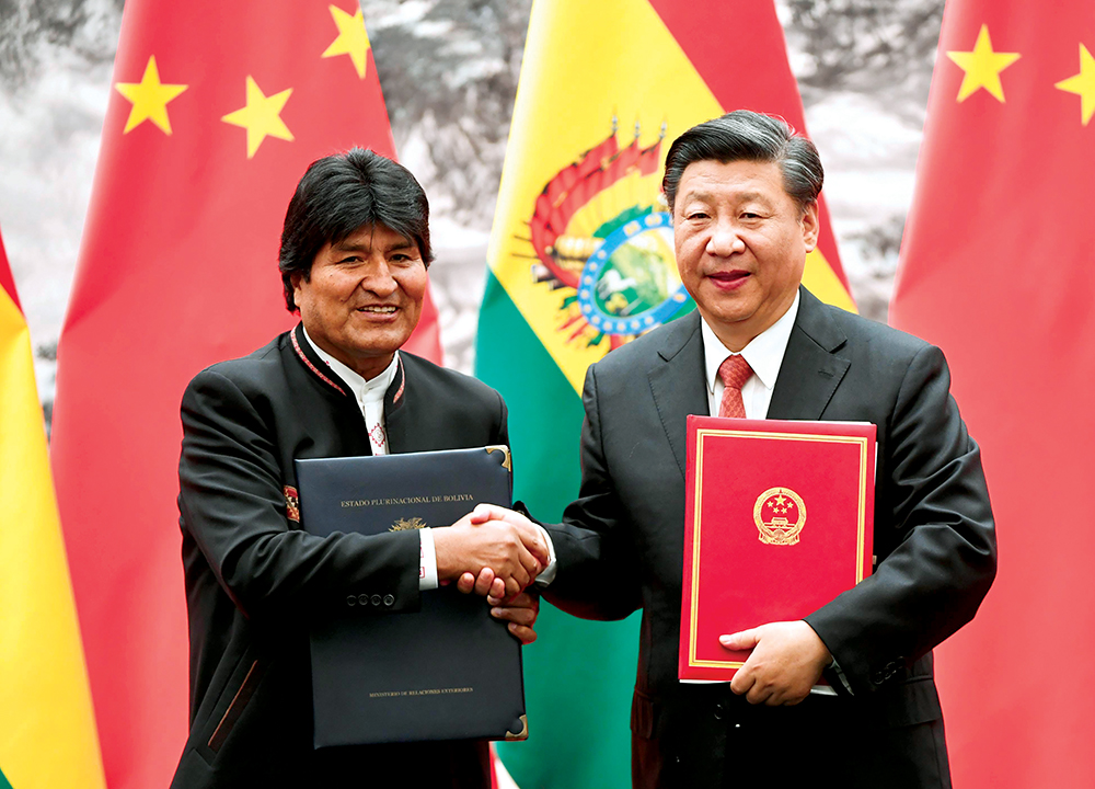 O Presidente da China, Xi Jinping, cumprimenta o Presidente boliviano Evo Morales no Grande Salão do Povo, em Pequim (Beijing), 19 Jun 18. A China pretende realizar investimentos expressivos na economia boliviana, sobretudo, em sua infraestrutura energética. A Bolívia é o único país sul-americano que abrange, concomitantemente, as regiões andina, platina e amazônica. (Kyodo via AP Images)