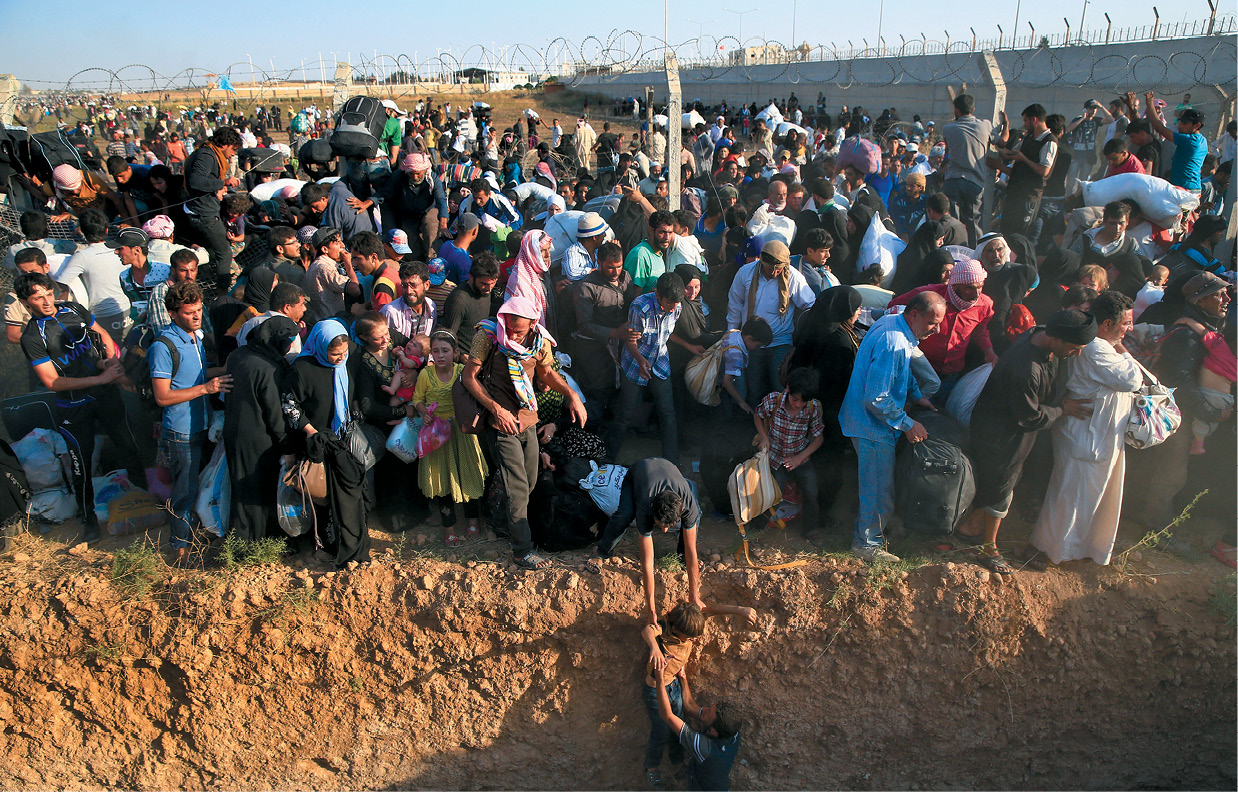 Refugiados caminham da Síria para Akçakale, Província de Sanliurfa, no sudeste da Turquia, após romperem uma cerca na fronteira, 14 Jun 15. O deslocamento em massa de sírios ocorreu quando os combatentes curdos anunciaram que estavam avançando em direção à cidade de Tal Abyad, bastião do Estado Islâmico perto da fronteira turca. (Foto de Lefteris Pitarakis, Associated Press)