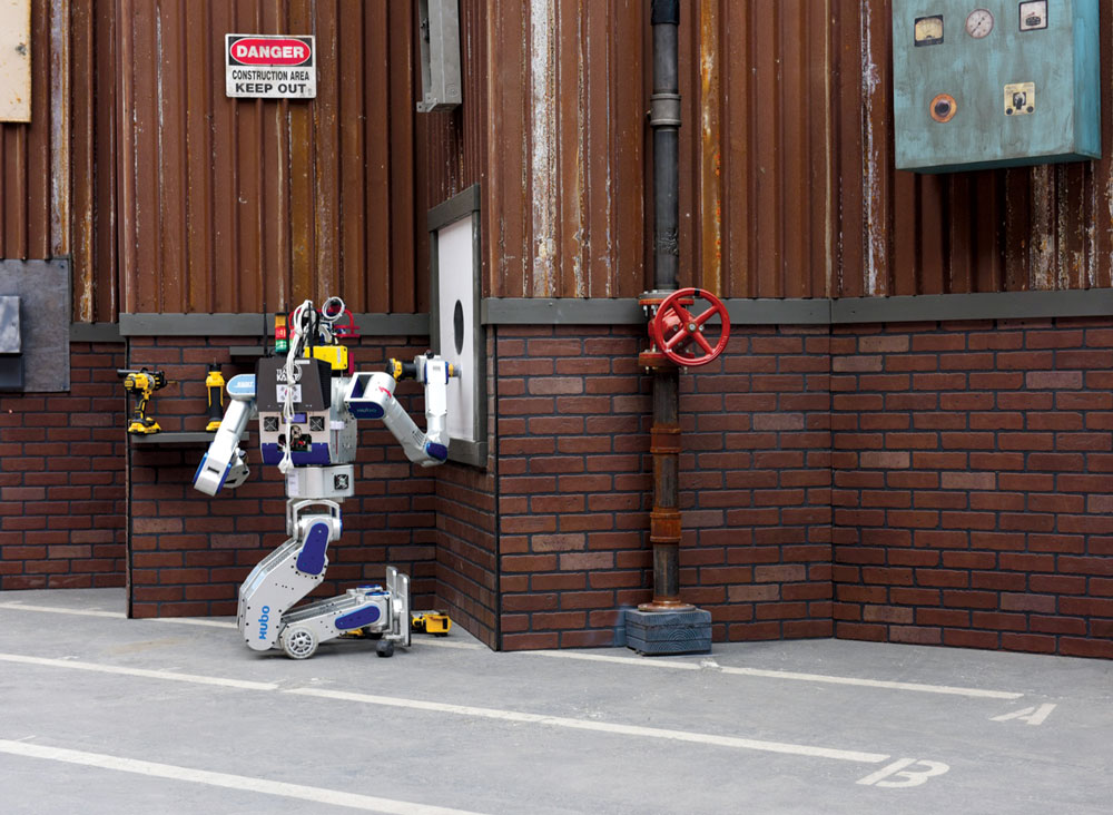 O robô vencedor da equipe Kaist, DRC-Hubo, utiliza uma ferramenta para perfurar uma parede na final da competição de robótica da DARPA, em Pomona, Califórnia, 4 Jun 2015. (Foto cedida pela DARPA)