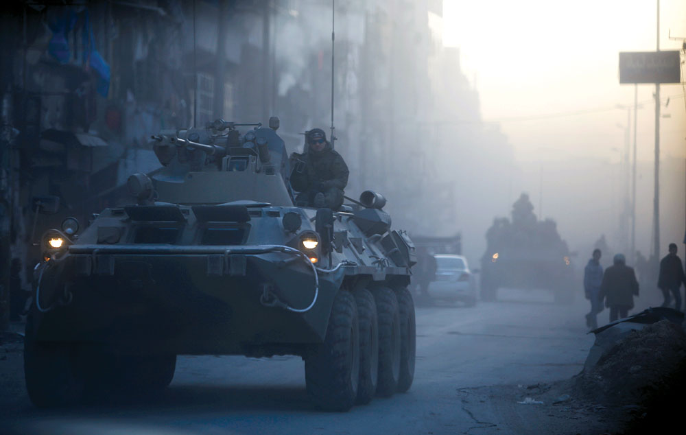 Militares russos em viaturas blindadas patrulham uma rua em Aleppo, na Síria, 2 Fev 2017. Os planejadores operacionais russos, ao que parece, limitaram o requisito de suas tropas terrestres, centrando-se, em vez disso, em preparar e apoiar o governo sírio e as forças iranianas a serem utilizadas como principais elementos de manobra e ataque. A presença russa em operações de combate envolveu, predominantemente, bombardeios aéreos, apoio aéreo aproximado, transporte e fogos indiretos a partir de elementos terrestres e navais, além de prover apoio logístico e de comunicações. (Foto de Omar Sanadiki, Reuters)