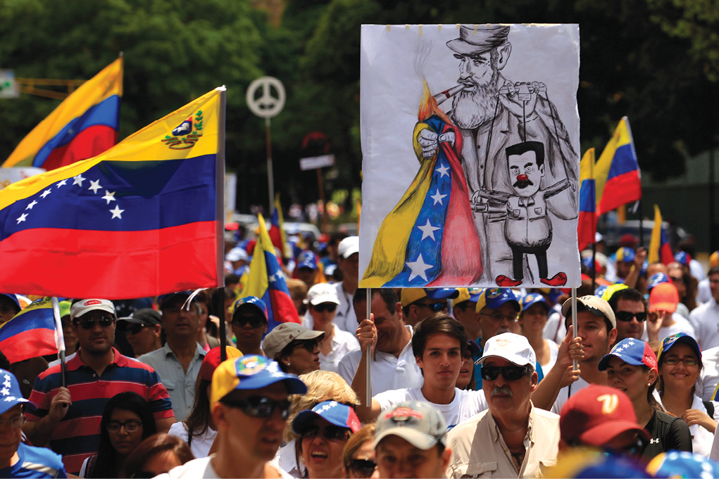 Cidadãos antigoverno realizam manifestações em 16 de março de 2014, em Caracas, na Venezuela, em parte para protestar contra a influência cubana dominante no governo do país. O Presidente Nicolas Maduro alertou os manifestantes para esvaziar a praça principal em Caracas ou enfrentar a remoção pelas forças de segurança. A Praça Altamira, no luxuoso leste de Caracas, foi o foco das manifestações antigoverno e violência que provocaram seis semanas de tumulto por toda a Venezuela, quando 28 pessoas foram mortas. (Tomas Bravo, Reuters)