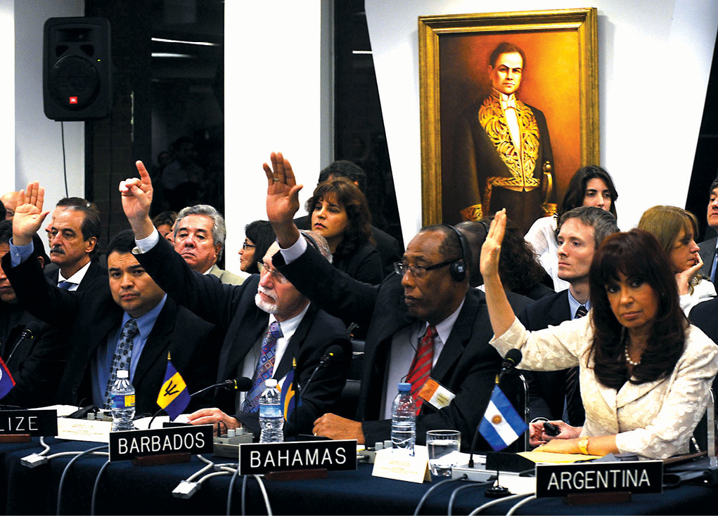 Representantes dos Estados membros da Organização dos Estados Americanos (OEA) votam para suspender a filiação de Honduras durante uma assembleia geral especial na sede da organização, em Washington, D.C., depois do golpe de Estado que expulsou do poder o Presidente hondurenho José Manuel Zelaya, 5 Jul 09. A OEA votou a readmissão de Honduras em 1 Jun 11, após Zelaya ter sido autorizado a voltar do exílio. Medidas semelhantes podem ser iniciadas contra a Venezuela (embora muitos Estados caribenhos na organização ainda apoiem a Venezuela em troca de subsídios petrolíferos). (Foto cortesia da Presidência da Nação de Argentina)