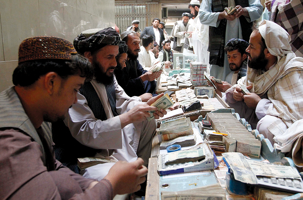 Cambistas afegãos trocam dinheiro em um mercado monetário na Província de Kandahar, 11 Nov 12. Esses mercados fazem uso frequente do hawala, um sistema tradicional de transferência de dinheiro usado extensivamente no Oriente Médio e na África, para movimentar grandes quantidades de fundos sem transferi-las fisicamente ou por meio de movimentação bancária por uma instituição financeira formal. Sob tal sistema, um cambista recebe dinheiro de um cliente em uma determinada localidade, que — por meio da cobrança de uma pequena taxa — incumbi um agente em um outro lugar de realizar o pagamento do valor acordado a um destinatário designado. Considerando que o sistema é relativamente informal, finalizado por um mero aperto de mão, torna-se difícil de ser monitorado. Como resultado, é frequentemente usado por terroristas ou outros agentes nefastos para transferir fundos globalmente. (Foto por Ahmad Nadeem, Reuters)