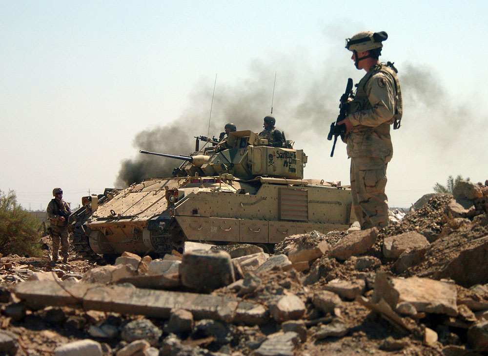 Integrantes do 2o Batalhão, 11o Regimento de Cavalaria Blindado, apoiados por uma viatura de combate Bradley, avançam cautelosamente para uma área de casamatas durante um ataque à fábrica de armas de Hateen, em Babil, Iraque, 26 Mar 2005. (Foto cedida pelo Departamento de Defesa dos EUA)