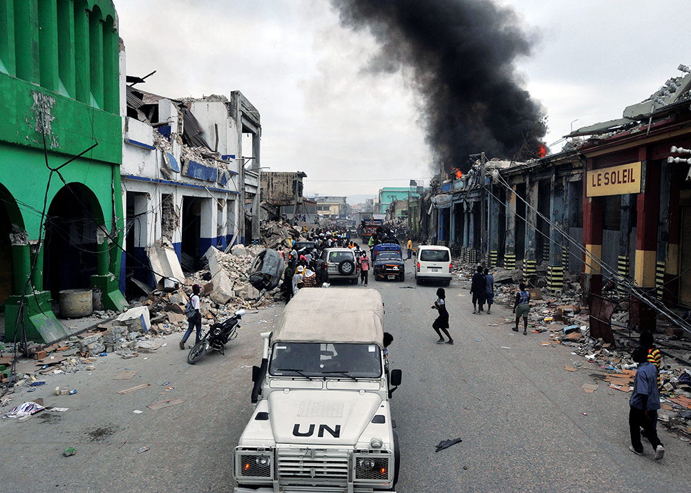 Veículo da ONU patrulha as ruas do bairro de Bel-Air, em Porto Príncipe, após o terremoto de 2010 no Haiti. O terremoto ocorreu às 16h53, horário local, em 12 Jan 10. Estima-se que 3 milhões de pessoas tenham sido afetadas e que 280 mil edifícios tenham sido gravemente danificados ou destruídos. (Foto: Marcello Casal Jr/ABr; obra derivada – Diliff, Wikimedia Commons, CC BY 2.5)