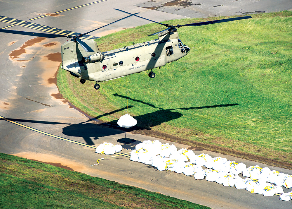 Um helicóptero CH-47 Chinook da Guarda Nacional transporta um grande saco de areia chamado de “supersaco” para colocação no vertedouro da represa Guajataca, 09 Out 17. O Corpo de Engenheiros do Exército dos EUA e a Guarda Nacional trabalharam em conjunto, a fim de estabilizar o vertedouro da represa após o dano causado pelo furacão Maria. (Sgt Mark Scovell, Exército dos EUA)