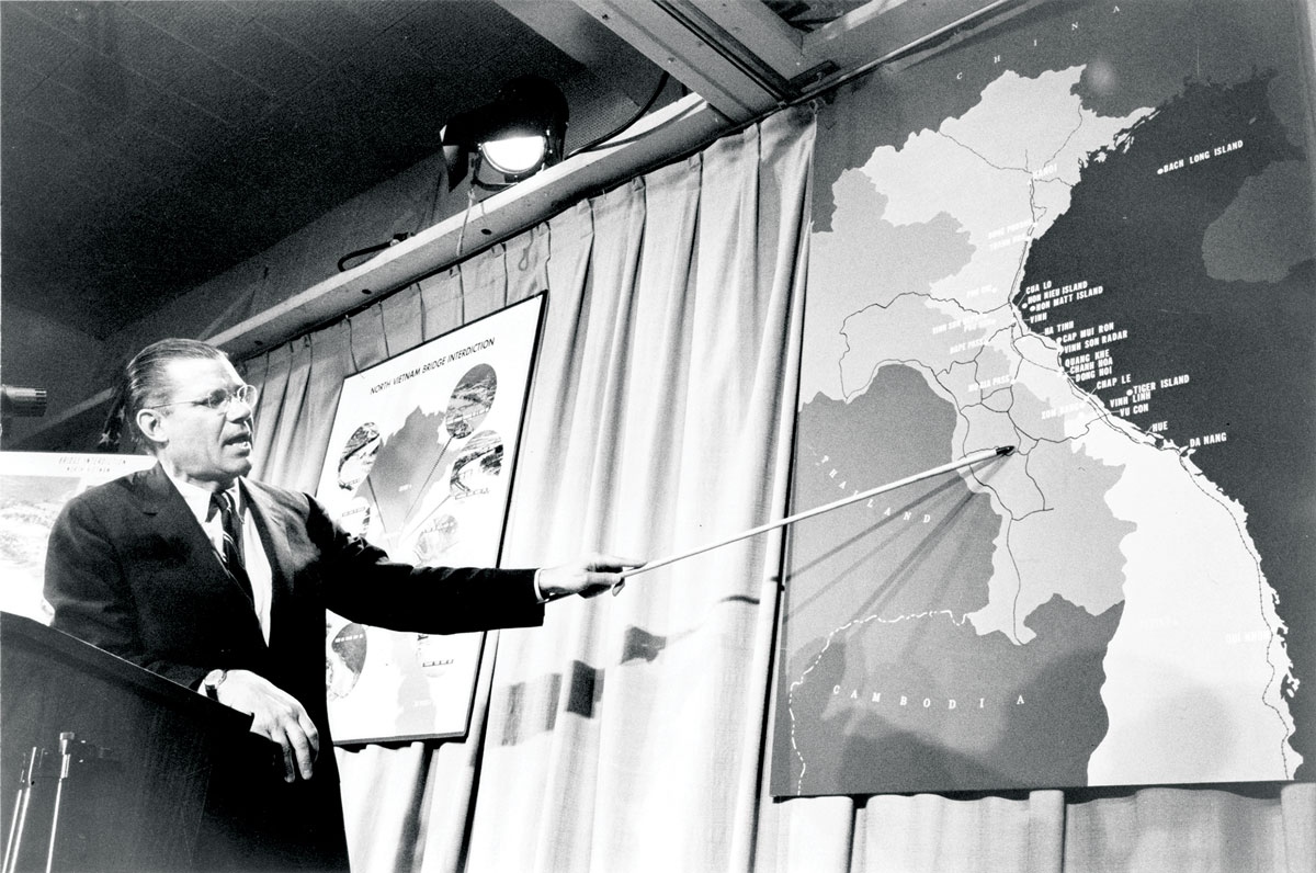 O Secretário de Defesa dos EUA, Robert McNamara, aponta para um mapa do Vietnã durante uma coletiva de imprensa em Washington, D.C., 26 Abr 1965. O planejamento estratégico e operacional para a condução da Guerra do Vietnã não descreveu, suficientemente, um estado final exequível, que levasse em consideração a história ou as condições sociais e geoeconômicas predominantes na nação dividida. (Foto da Biblioteca do Congresso dos EUA)