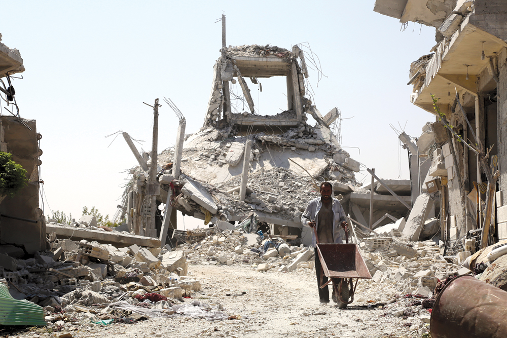 Un hombre empuja una carretilla frente a edificios derrumbados en Manbij, norte de Siria, el 14 de agosto de 2016. Muchos regresaron a sus hogares después de que Fuerzas Democráticas Sirias y fuerzas especiales de EUA liberaran la ciudad del Estado Islámico. (Foto: Delil Souleiman, Agence France-Presse)