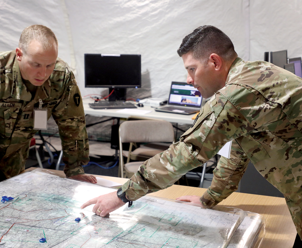 El mayor Alex J. Duffy (der.), oficial de operaciones del 3er Equipo de Combate de Brigada de la 10a División de Montaña y el capitán Jacob M. Allen, el segundo jefe de operaciones, usan un mapa superpuesto con gráficas operacionales para apoyar los sistemas digitales de mando tipo misión y proporcionar la redundancia, 17 de septiembre de 2018, durante el ejercicio Cyber Blitz 2018 en la base conjunta McGuire-Dix-Lakehurst, New Jersey. Este método alternativo se convirtió en el medio principal para seguir el combate temporalmente cuando un ciberataque desactivó los sistemas. (Foto: U.S. Army Communications-Electronics Research, Development and Engineering Center)