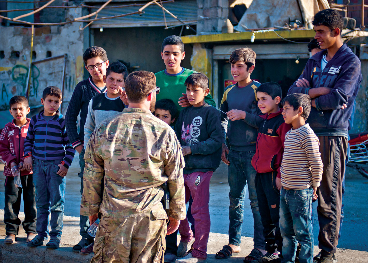 Un soldado de la coalición habla con niños en un mercado en Raqqa, Siria, 13 de marzo de 2018. La reaparición de vendedores en los mercados sirios es una señal de un regreso a la normalidad después de la derrota del Estado Islámico por las Fuerzas Democráticas Sirias. (Foto: Ejército de EUA, Sgto. 2o Timothy R. Koster)