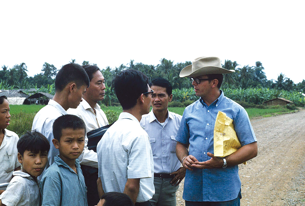 Bill Graham (der.) discute un proyecto para reabrir el canal de la aldea de Thạnh Phú, en enero de 1970, en el distrito de Châu Thành, Vietnam. Durante la construcción de una base para la 9a División de EUA en Đồng Tâm, el canal quedó cubierto y el Ejército de EUA se rehusaba a dragarlo. Por ello, mediante el apoyo del programa de Operaciones Civiles y Desarrollo Rural (CORDS), incluyendo fondos y productos alimenticios, se compensó a los pobladores para que ayudaran a retirar el sedimento del canal. El canal tenía una extensión de casi un kilómetro y tomó casi tres meses para finalizar este proyecto. (Foto: American Foreign Service Association/The Foreign Service Journal, http://afsa.org/sites/default/files/flipping_book/0415/files/assets/basic-html/page-1.html)