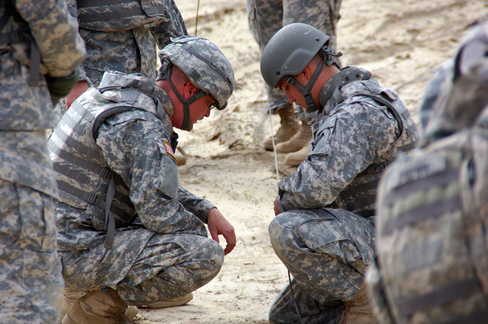 Staff Sgt. Justin Creswell, left, an 89B course instructor at Fort McCoy, Wis., helps Spc. Scott Harris tie a girth hitch with an extra turn to connect a transmission line to the main line before a demolition blast. The class spent the day at a demolition range learning how to safely do demolition blasts. (Photo by Jonathan (Jay) Koester / NCO Journal)