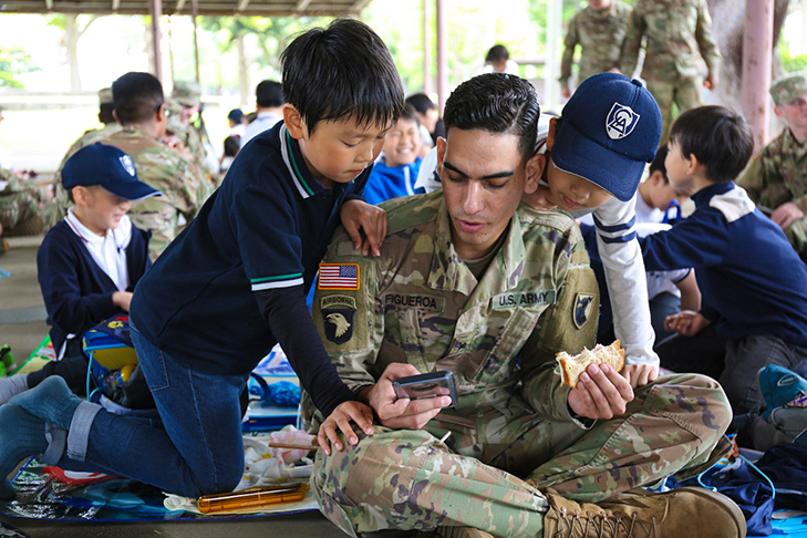 A Soldier assigned to the 38th Air Defense Artillery Brigade, shows LCA Kokusai Elementary School students a game on his cellphone
