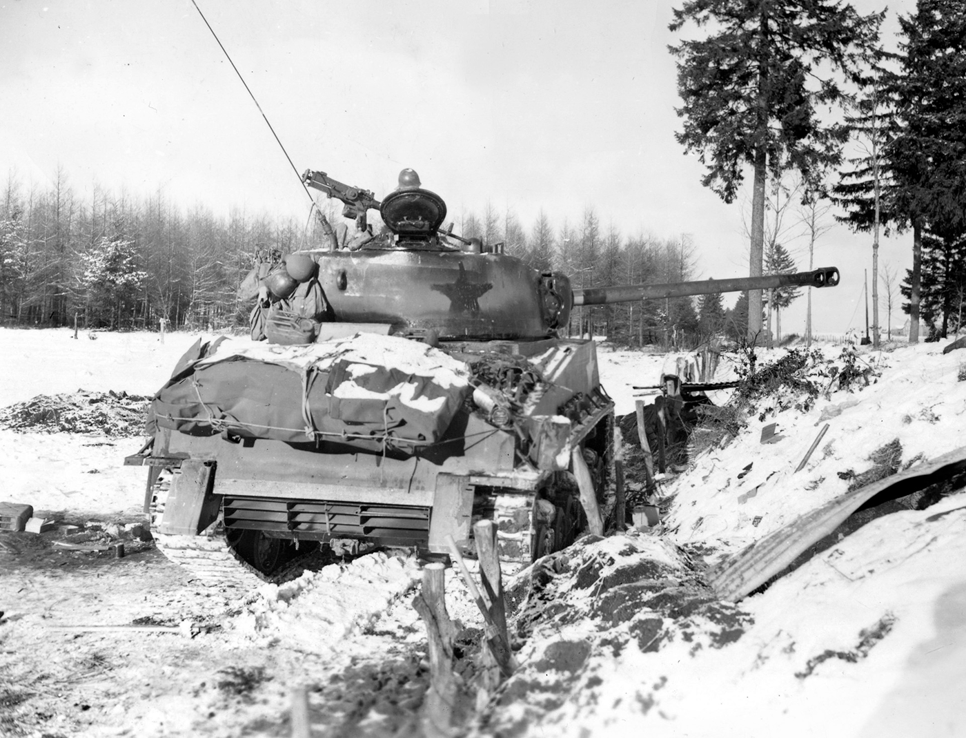 A horizontal photograph shows a tank with a star on its turret, rolling through a snowy landscape beneath a white sky. The image is black and white, with trees rising from a distant horizon beyond the vehicle. This image is the second in a series of 12 accompanying the article.