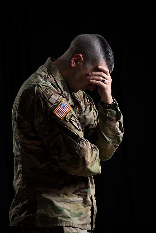 Against a black backdrop, a bareheaded Soldier casts his head down and covers his face with his hand — a pose suggesting sorrow and dejection.